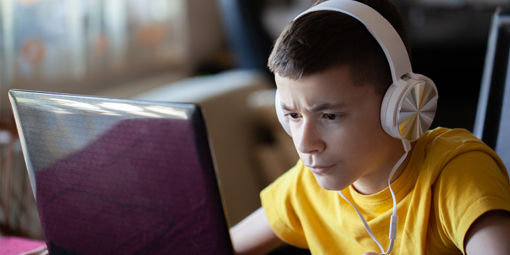 a student wearing headphones and concentrating at what is displayed on their laptop