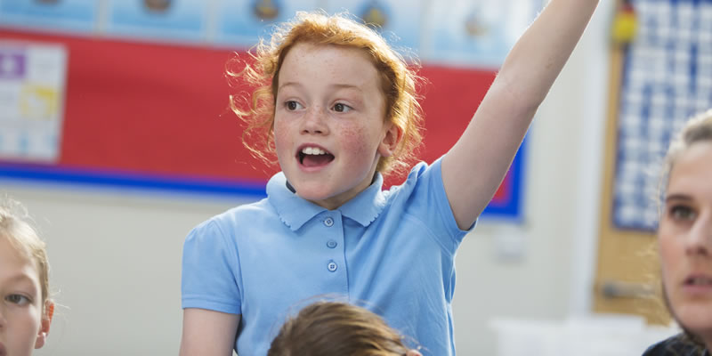 young school girl with her hand in the air to answer a question