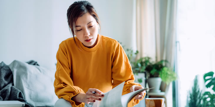 young woman reading book and making notes at home