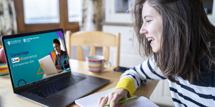 Teacher sitting at a kitchen table watching the Cambridge Live Experience conference in a laptop 