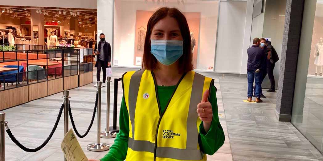 Cambridge Assessment colleague and volunteer Claire holding clipboard with thumbs up and wearing high visibility jacket