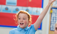 young school girl with her hand in the air to answer a question