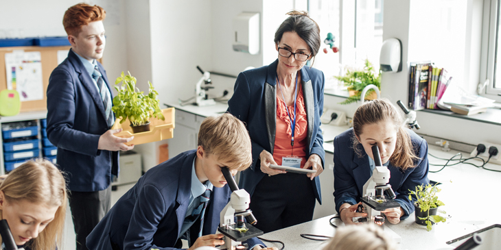 Secondary schools students studying with microscopes with a woman teacher next to them