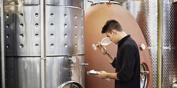 Man smelling wine in front of wine barrels