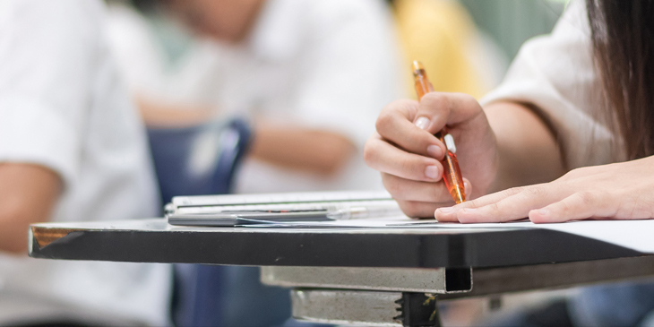 Close-up of student taking a written exam paper sitting at a desk in an exam hall
