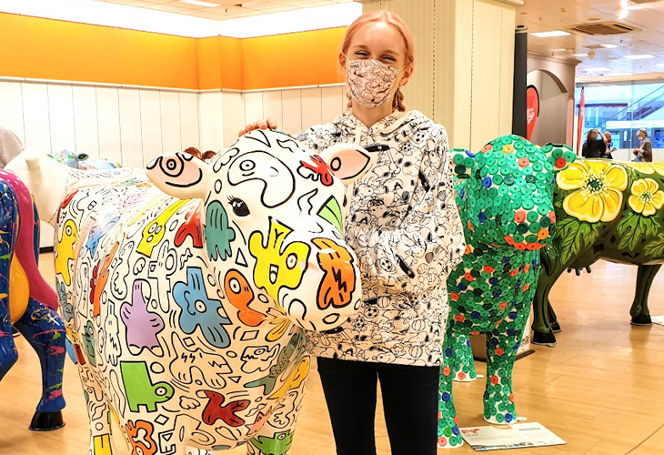 Young artist Tori Woolley with the cow called Yoodle Moodle that she painted for Cambridge Assessment as part of the Cows About Cambridge outdoor art trail