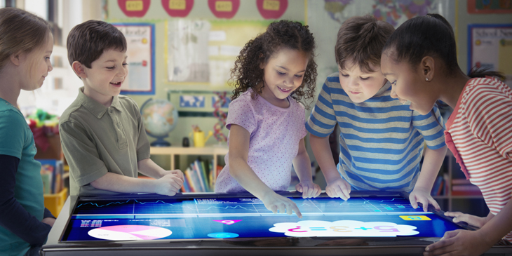 Group of primary school children in a classroom using a table top touch screen display