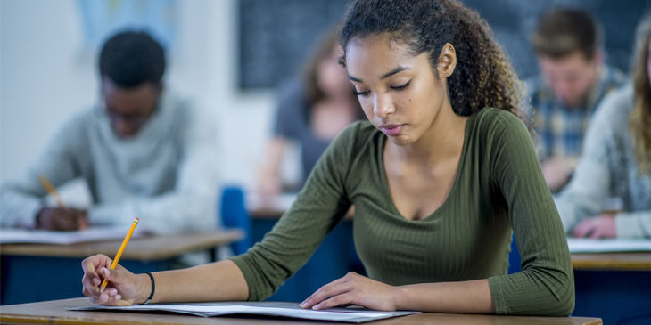 Female student taking a written exam paper sitting at a desk in an exam hall