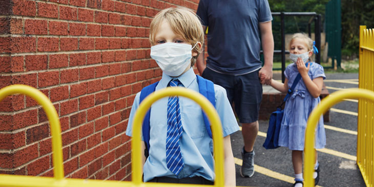primary children approaching a school gate dressed in uniforms and wearing face masks