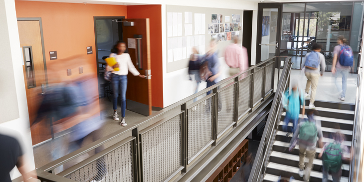 A blurred photo of a school corridor and stairway with students moving between rooms