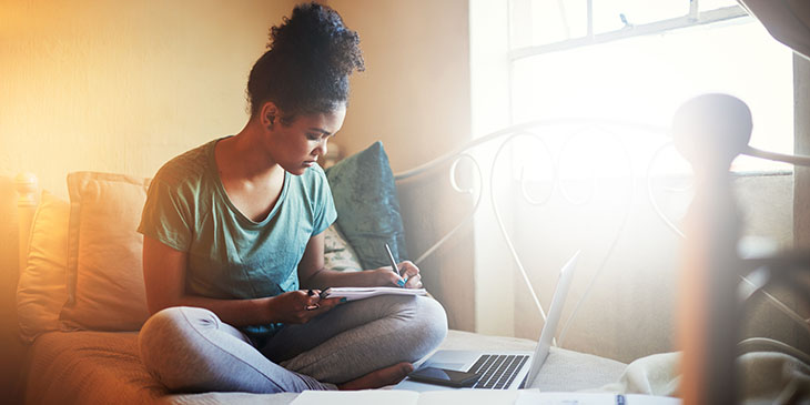 student sitting on a bed studying