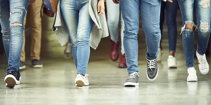 The legs of students walking forwards along a corridor