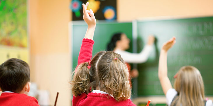 Child wearing red jumper putting hand up in class