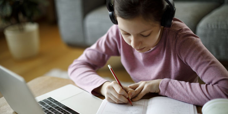 Teenage student studying on their own at home using a laptop headphones pen and paper