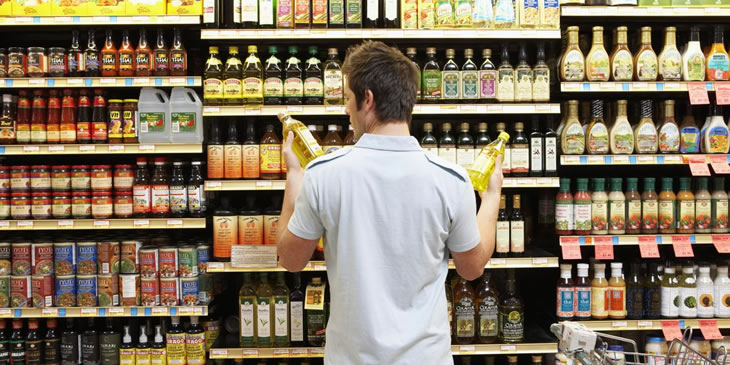 Young man in supermarket comparing bottles of oil